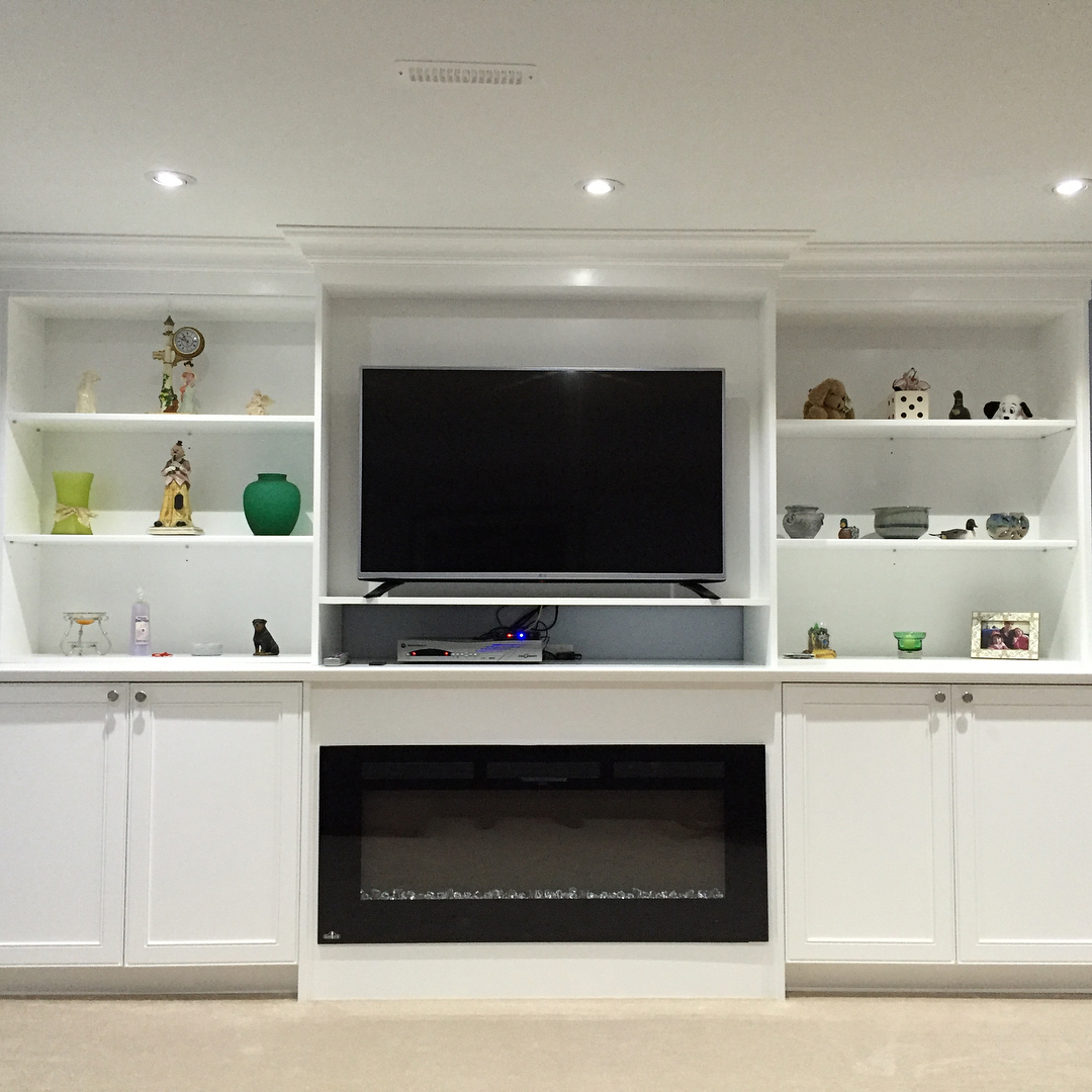 Finished basement with white built-in media wall and electric fireplace — Reno-eX renovation